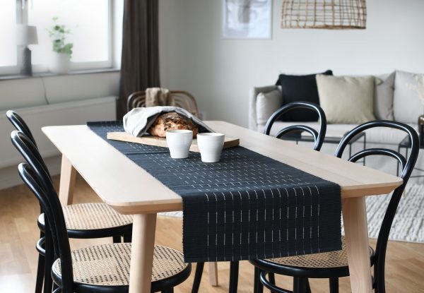 Krásny dizajnový behúň na stôl z organickej bavlny v čiernej farbe s jemnými bielymi prerušovanými pruhmi.