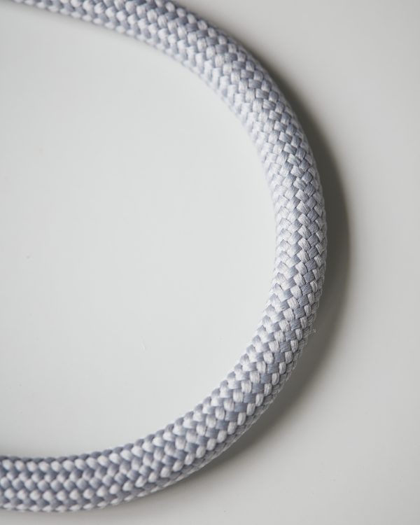 Minimalistický okrúhly kovový vešiak potiahnutý nylónom v sivej farbe.
